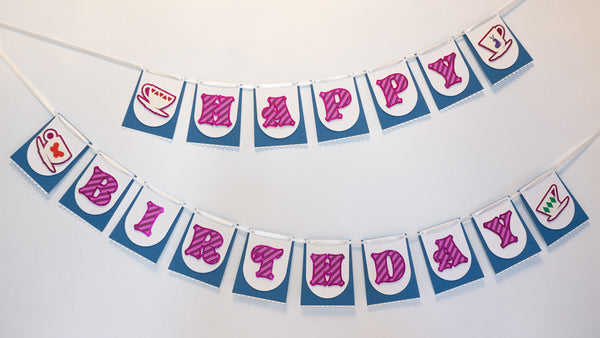 A handmade Alice in Wonderland birthday banner hanging on a white wall. It's in two sections & made up of individual paper pennants that resembles a blue skirt & white apron, just like Alice's. The skirt-like pennants in the first section have letters that spell "HAPPY." The second section spells "BIRTHDAY." The letters are a whimsical font & are striped pink like the Cheshire Cat. The pennants on the ends of each section feature 4 different teacups with hearts, diamonds, a rabbit & a butterfly.
