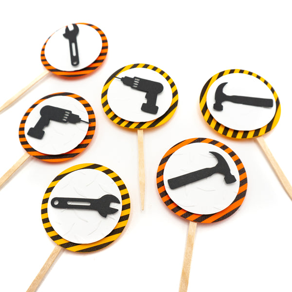 Six cupcake toppers with black tools on top of a white circle of embossed diamond plate cardstock, which is placed on top of a circle of warning stripe paper.