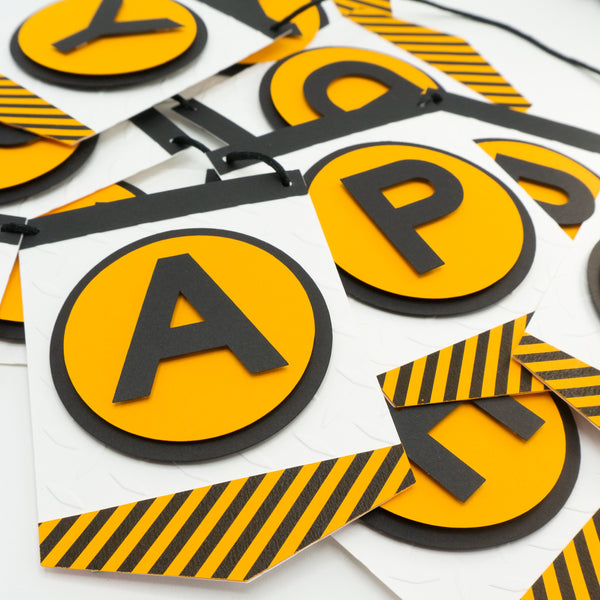 A close-up of a construction zone themed happy birthday banner. This photo shows off the letters which are all on an orange circle and on a separate pennant. Strung on a black cord.
