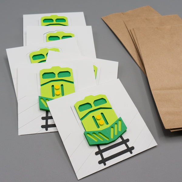 Small paper bag party favor bag with freight train themed header card attached. The header card features a head-on view of a freight train engine. In this picture that are unassembled.
