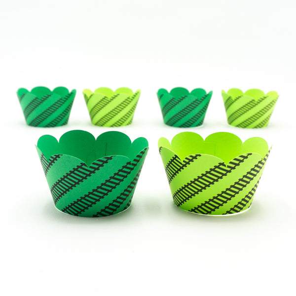 Bright green cupcake wrappers in two shades. Black railroad tracks wrap around at an angle. And the top edge of the wrapper is scalloped.