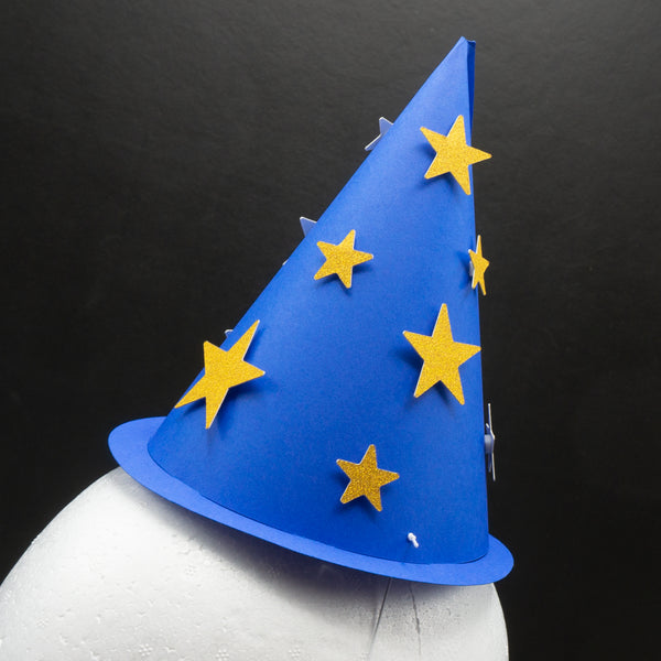  single blue cone-shaped wizard party hat with a thin brim is shown on a white mannequin head against a black background. The hat resembles a classic wizard costume accessory and is decorated with scattered gold glitter star cutouts of varying sizes.
