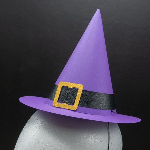 A standard cone-shaped paper party hat, resembling a witch hat, on a styrofoam head dummy. Complete with a wide brim and a buckled hat band. The hat is purple, with a black pleather band, and a gold glittery buckle.