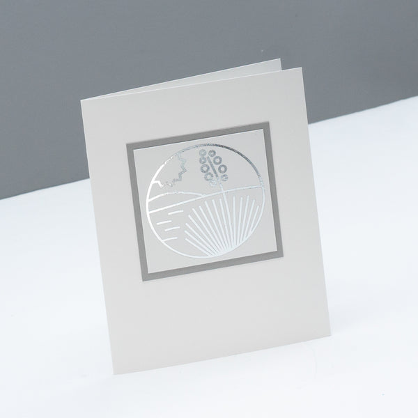 Note card with a modern monoline style drawing of a yucca in the desert with a hill in the background and the sun in the sky. the line drawing is foiled in a metallic silver..