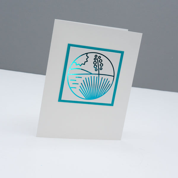 Note card with a modern monoline style drawing of a yucca in the desert with a hill in the background and the sun in the sky. the line drawing is foiled in a metallic turquoise color.