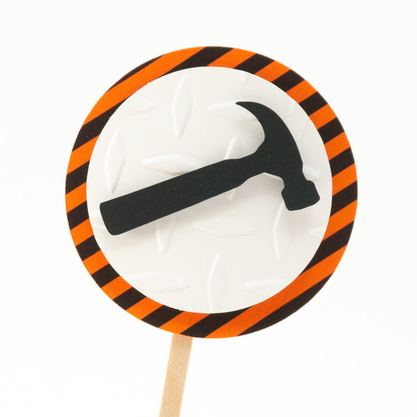 A cupcake toppers with a black hammer on top of a white circle of embossed diamond plate cardstock, which is placed on top of a circle of warning stripe paper.