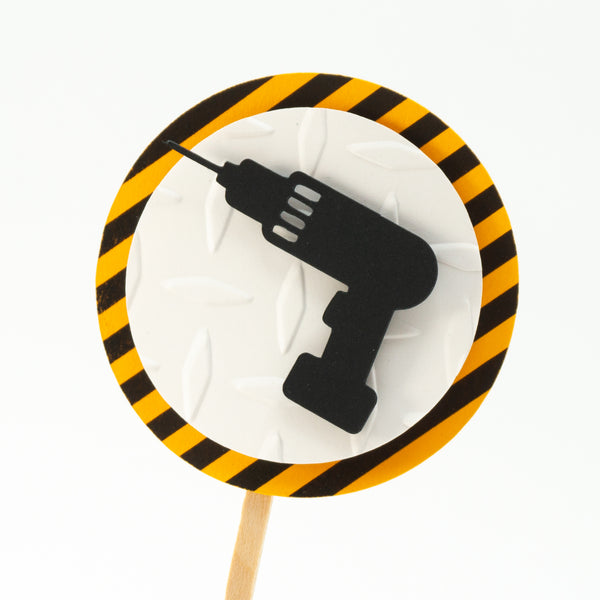 A cupcake toppers with a black drill on top of a white circle of embossed diamond plate cardstock, which is placed on top of a circle of warning stripe paper.