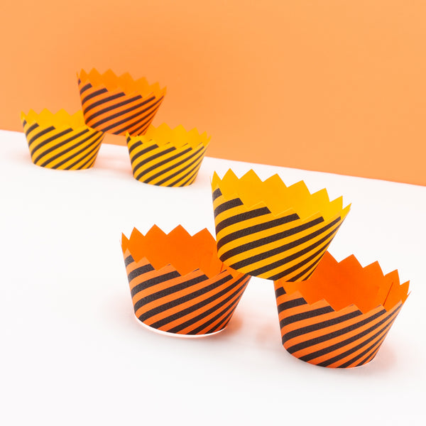 Black and orange striped cupcake wrappers to resemble caution tape. The top of the wrapper has a zig-zag edge. They are photographed stacked on top of each other.
