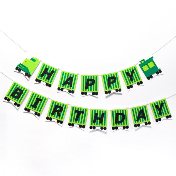 A straight on photo of the birthday banner hanging on the wall. It’s fashioned to look like a green freight train. Each pennant is a cargo car with one letter on it. 