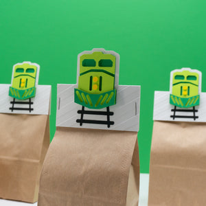 Small paper bag party favor bag with freight train themed header card attached. The header card features a head-on view of a freight train engine.