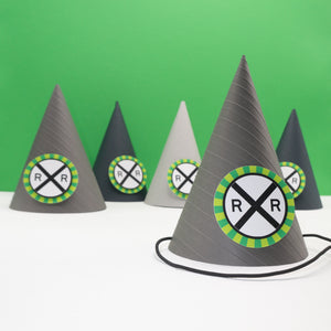 Gray party hat with embossed stripes and a railroad crossing sign on the front. The sign is bordered with a burst of green. 