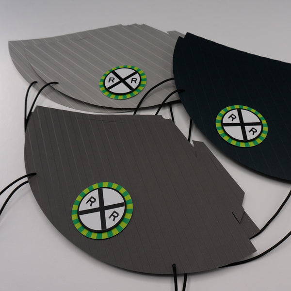 Gray party hats with embossed stripes and a railroad crossing sign on the front. The sign is bordered with a burst of green. The hats are pictured flat, before being formed into cones.